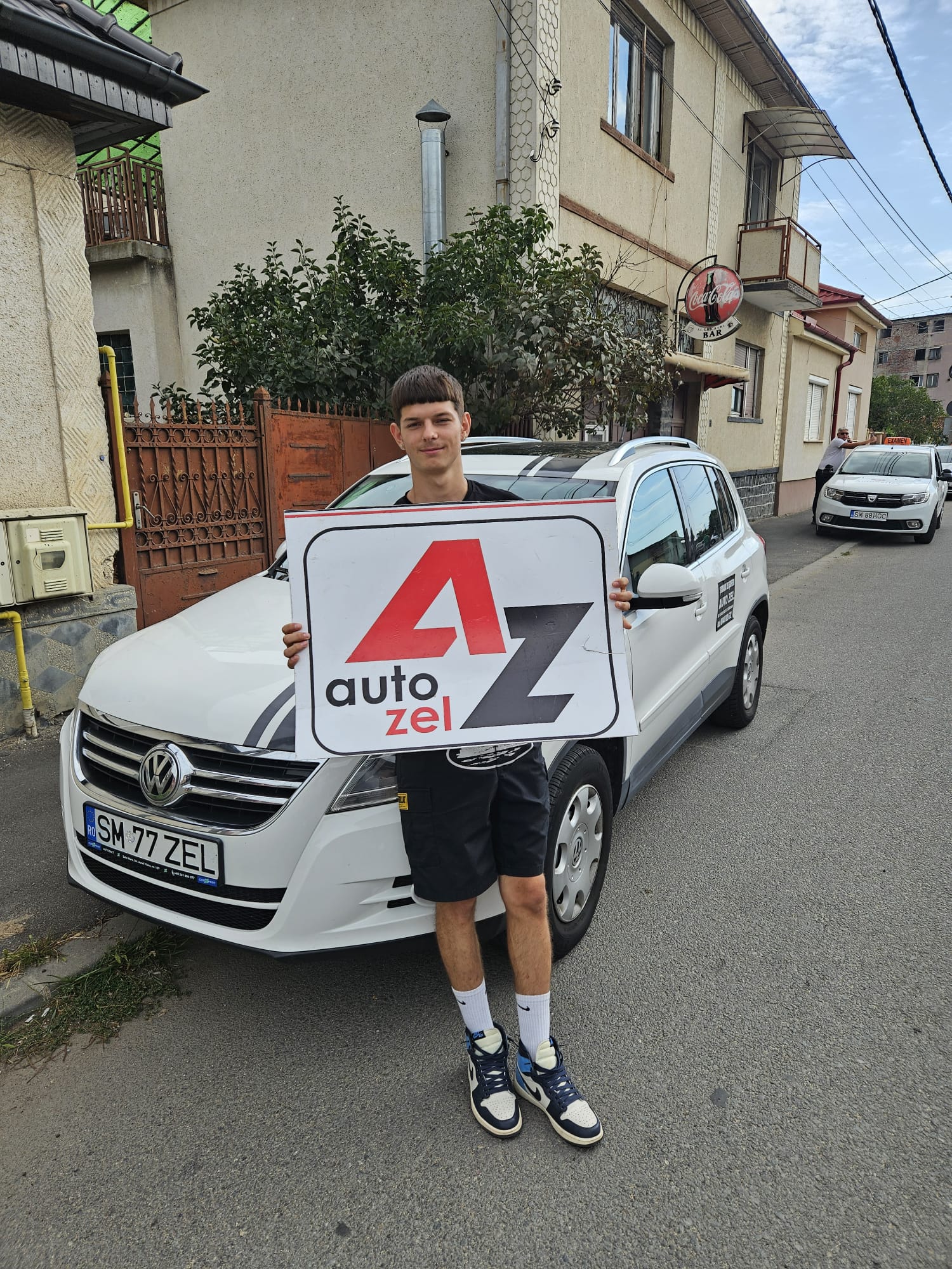 Cursant Auto Zel ținând placa AZ în fața VW Tiguan după examen