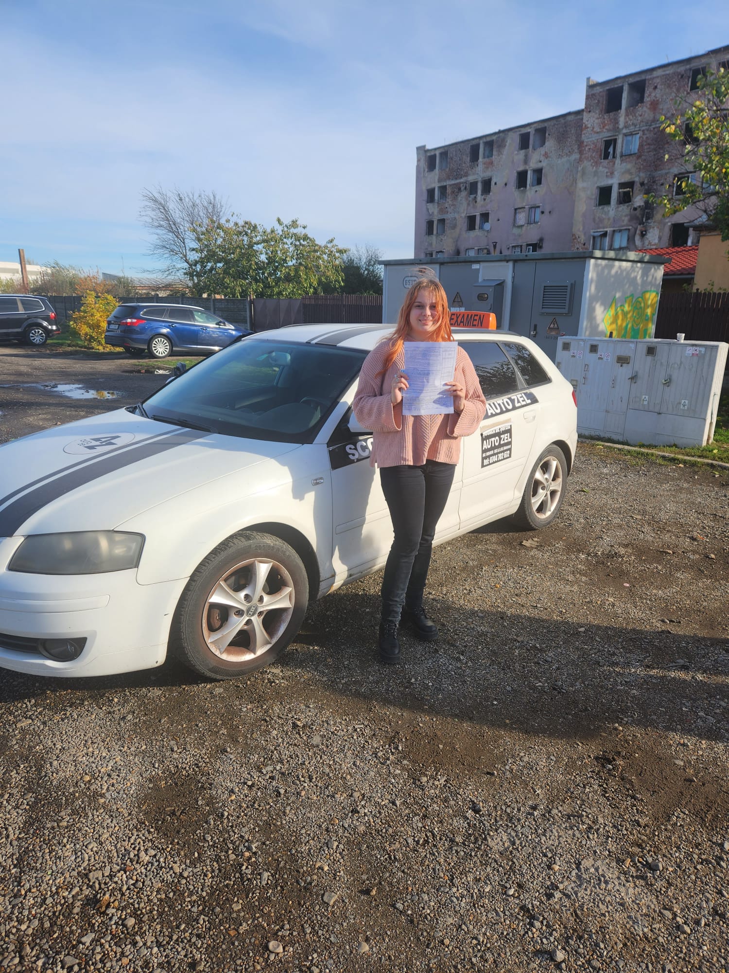 Cursantă Auto Zel cu foaia de examen lângă Audi A3 al școlii