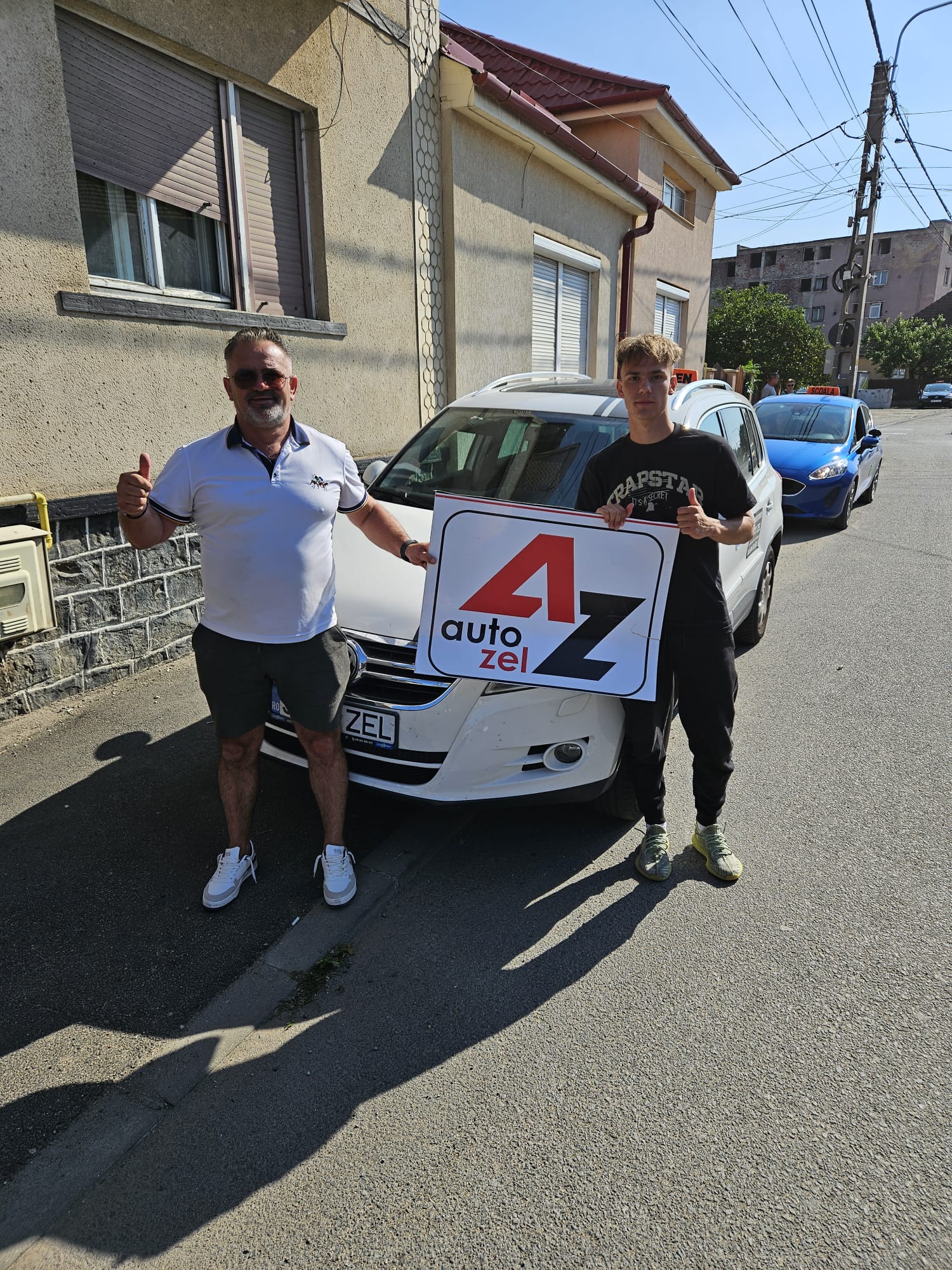 Instructorul Auto Zel și cursantul cu placa AZ lângă mașina școlii
